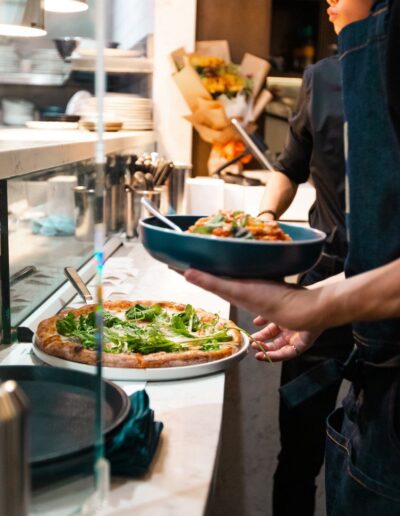 A man in an apron is serving a pizza to a customer.