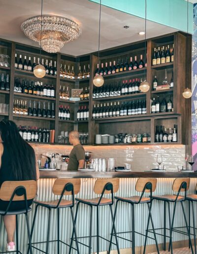 A woman sits at a bar with wine bottles in front of her.
