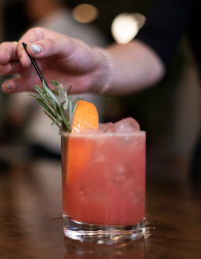 A person is preparing a cocktail with an orange garnish.